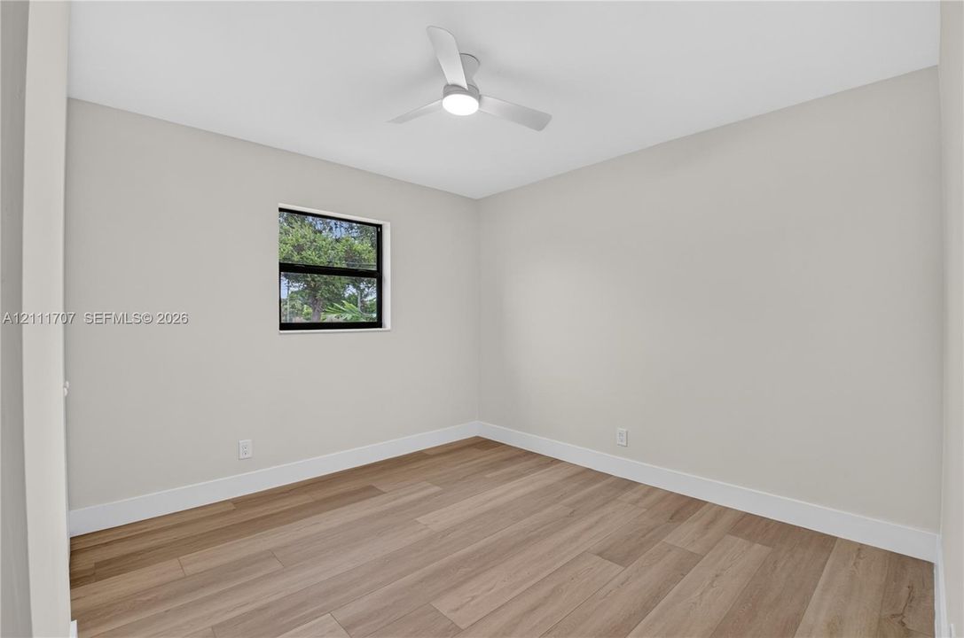 Neutral-toned walls, wood-finish flooring, and a modern ceiling fan with integrated lighting, featuring a single window with black framing