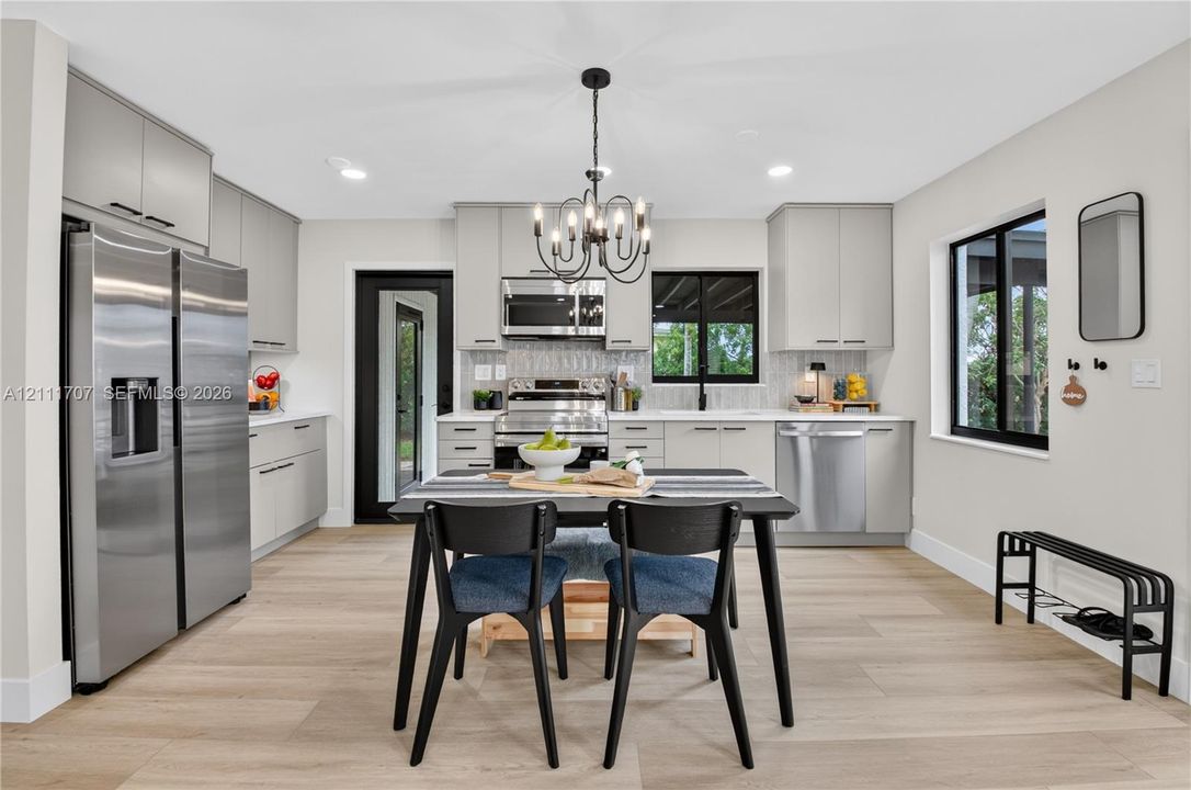 Kitchen featuring light beige cabinetry, stainless steel appliances, wood-finish flooring, a multi-arm chandelier, and a black-framed exterior door