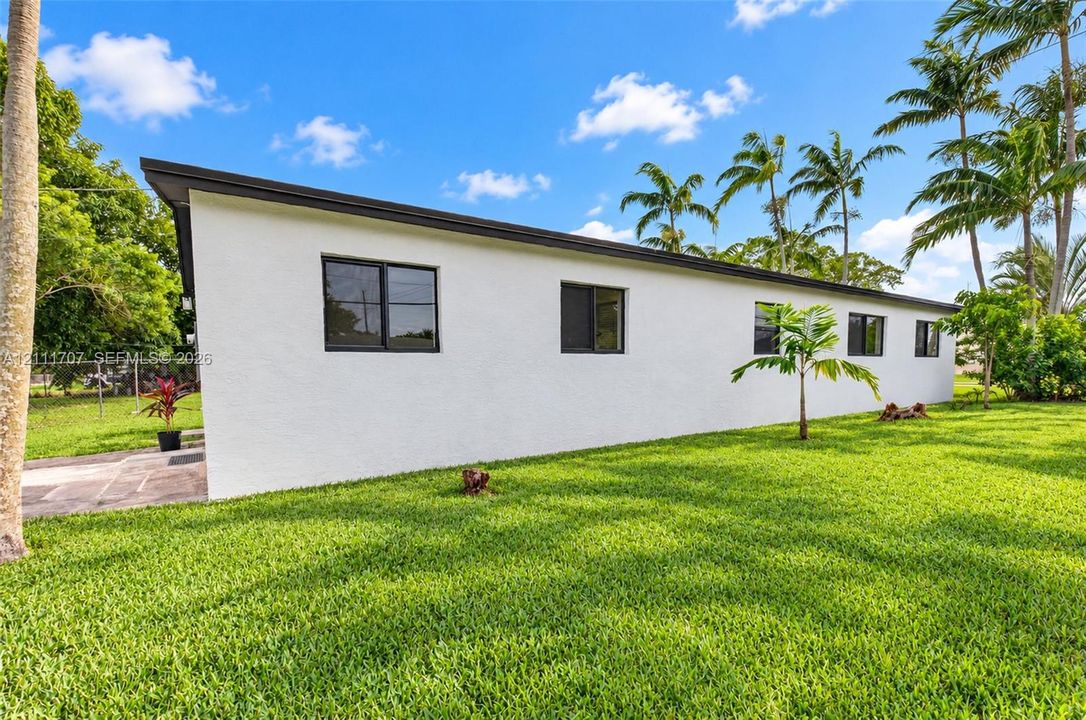 Exterior profile featuring white stucco siding, a flat roofline, dark-framed windows, and expansive green lawn