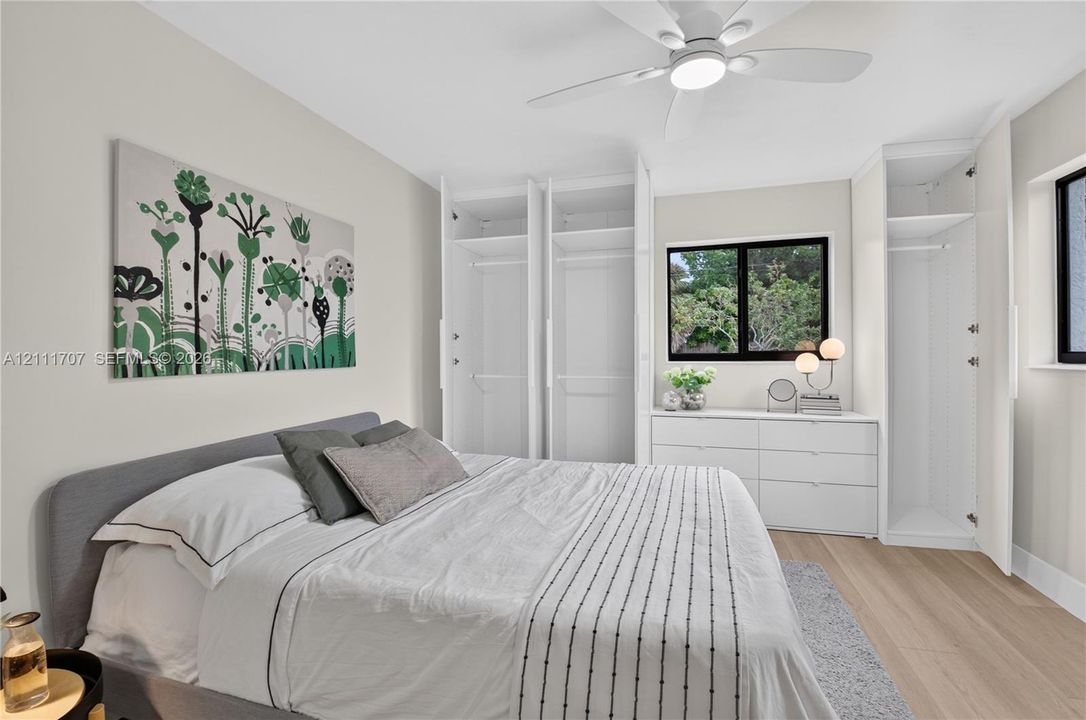 Built-in floor-to-ceiling closet cabinetry, light-toned wood-finish flooring, dual-pane windows with dark frames, and a modern ceiling fan with integrated lighting