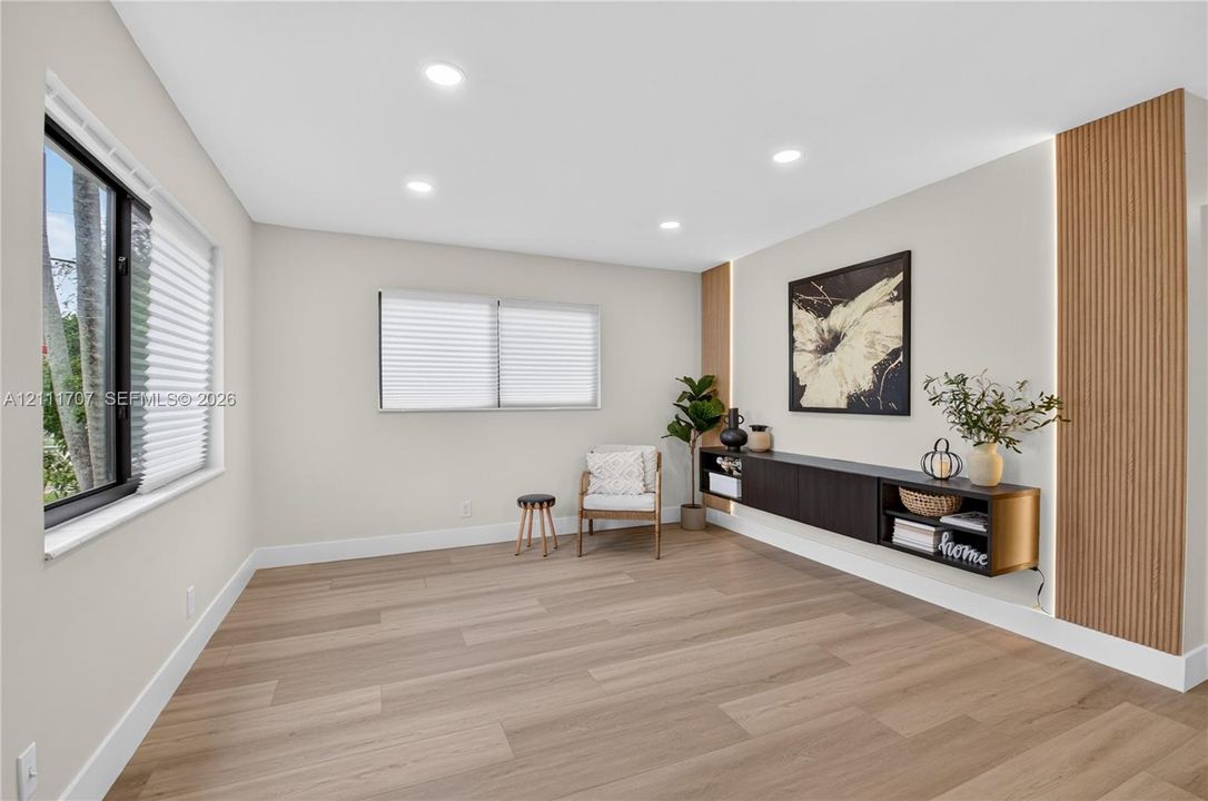 Living area featuring light wood-finish flooring, recessed lighting, horizontal slider windows, a wall-mounted floating cabinet, and vertical wood-slat accent panels with integrated lighting