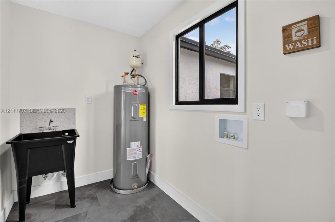 Utility area featuring slate-style flooring, a deep basin utility sink with a stone-finish backsplash, and a dedicated water heater