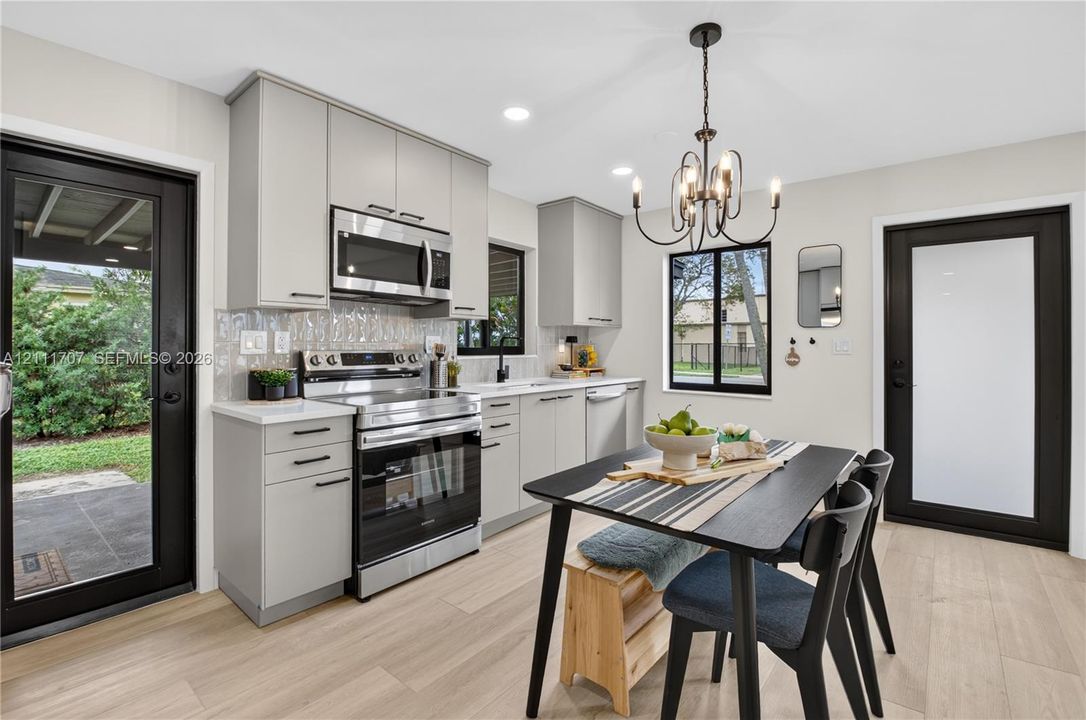 Kitchen featuring beige flat-panel cabinetry, stainless steel appliances, a textured tile backsplash, wood-finish flooring, and a multi-light chandelier