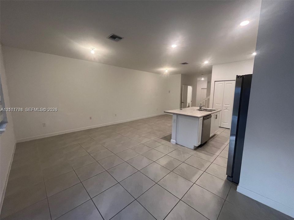 Open-concept interior featuring large-format ceramic tile flooring, recessed ceiling lighting, a kitchen island with a stone-surface countertop, and stainless steel kitchen appliances
