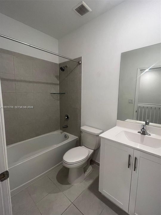 Bathroom featuring a white vanity cabinet with a rectangular basin, polished chrome faucet, large frameless mirror, and a tile-surround bathtub
