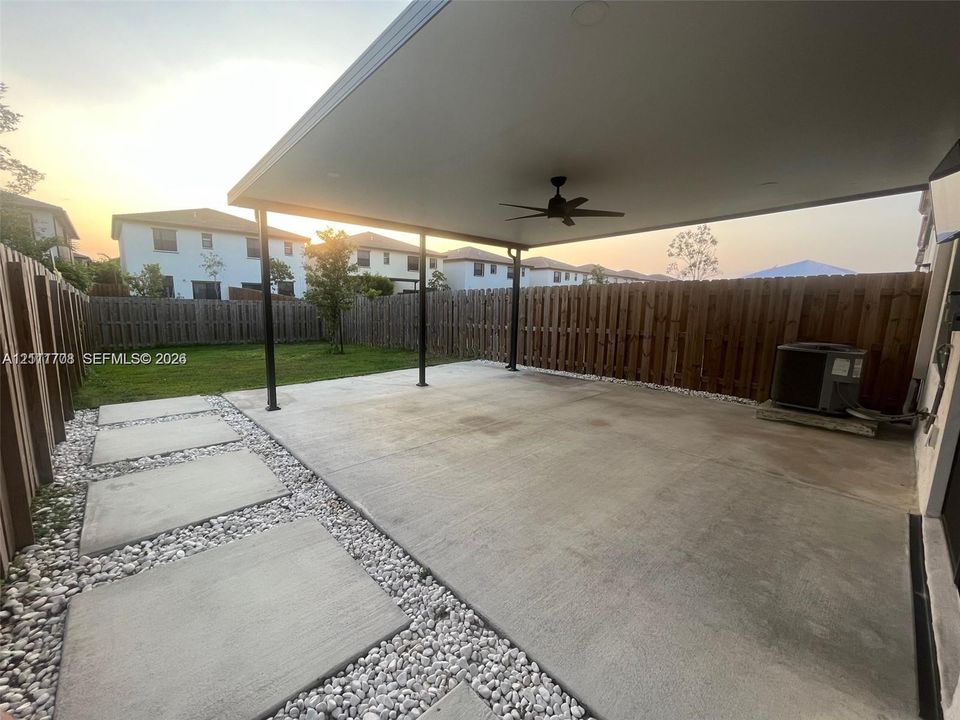 Covered concrete patio featuring a ceiling fan, wood-style privacy fencing, and concrete paver walkway set in decorative stone