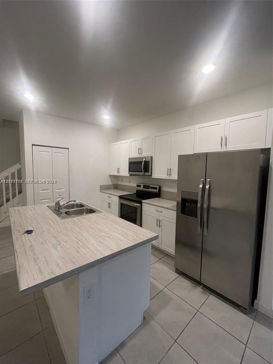 Kitchen featuring white shaker-style cabinetry, wood-finish countertops, stainless steel appliances, recessed ceiling lighting, and tile flooring