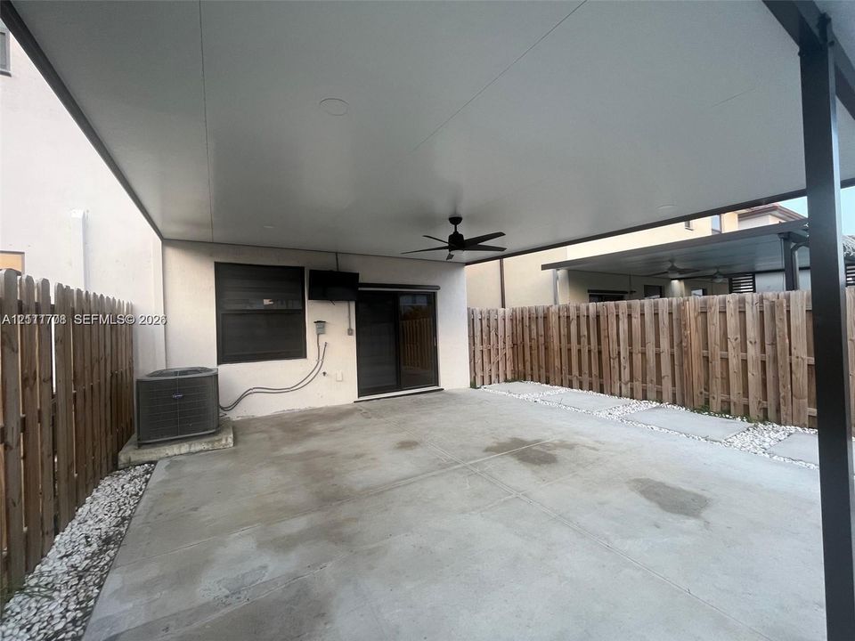 Covered outdoor patio featuring concrete flooring, a ceiling fan, sliding glass door access, and a wood privacy fence