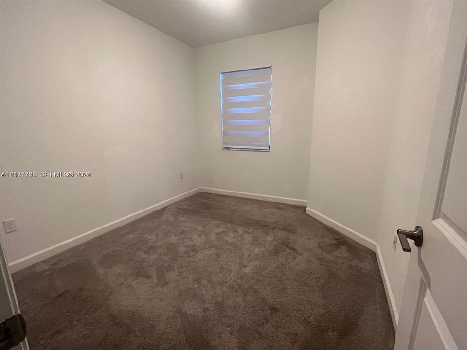 Neutral-toned interior room featuring wall-to-wall carpeting and a window equipped with horizontal shade blinds