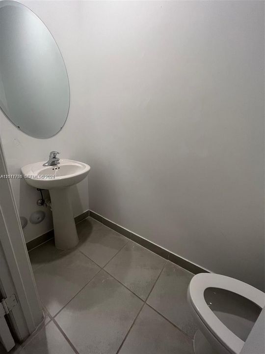Pedestal sink with a single-handle faucet, oval frameless wall mirror, and large-format tile flooring