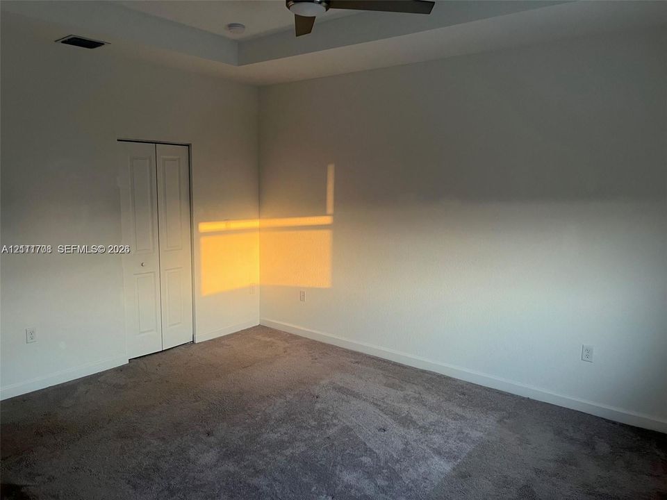 Room featuring neutral carpeting, a tray ceiling, a ceiling fan, and bi-fold closet doors