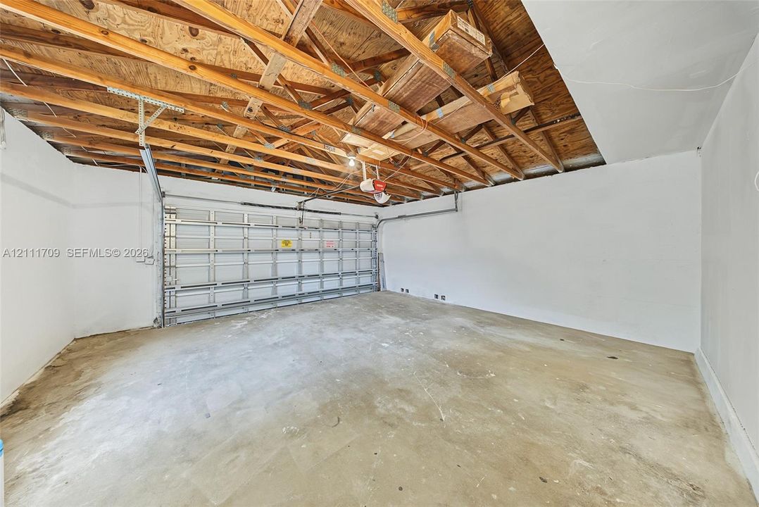 Garage interior featuring exposed rafter framing, white-painted walls, concrete flooring, and a sectional metal garage door