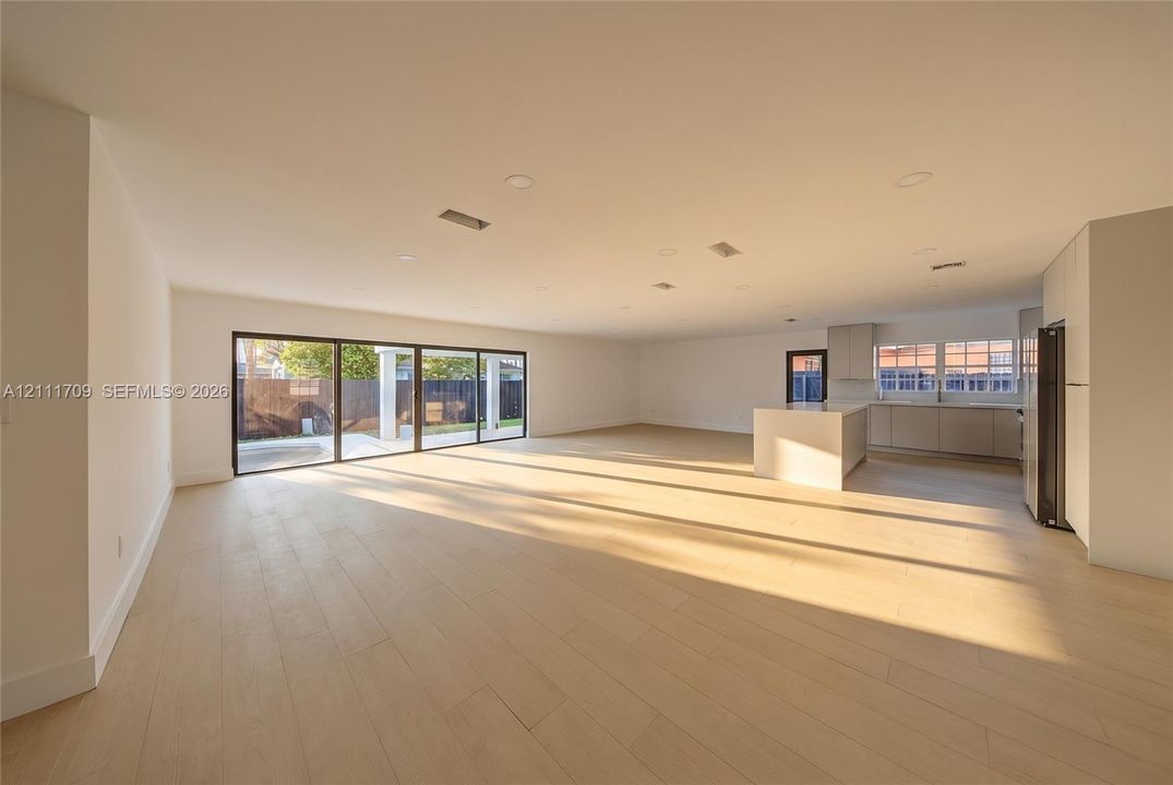 Open-concept floor plan featuring wood-finish flooring, recessed lighting, multi-panel sliding glass doors, and a central kitchen island with integrated cabinetry