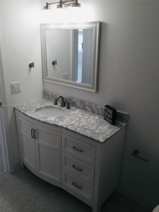 White shaker-style vanity with stone-patterned countertop, integrated basin, brushed metal hardware, and framed wall mirror