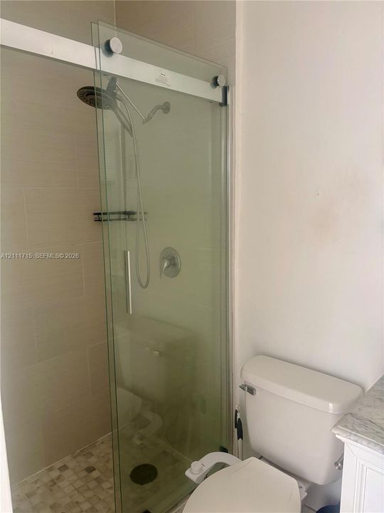 Walk-in shower with a sliding glass door, rainfall showerhead, and a handheld wand, featuring neutral wall tiling and a square-tile mosaic floor
