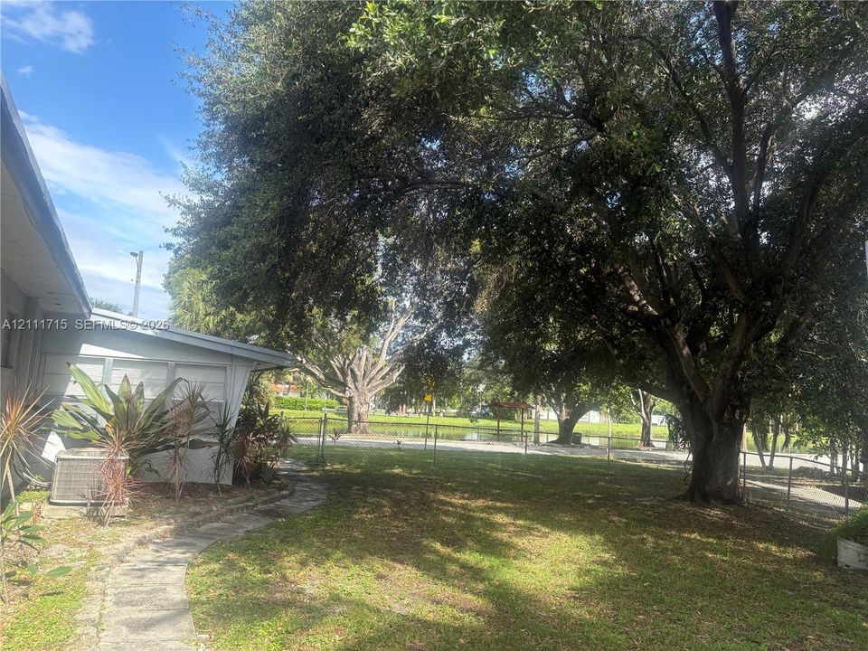 Outdoor space featuring mature trees, a stone pathway, chain-link fencing, and water frontage