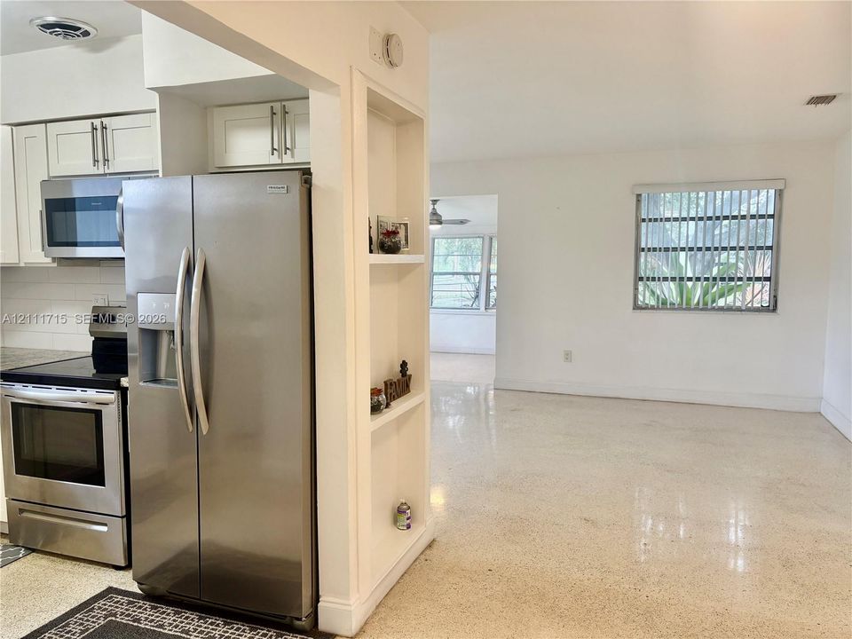Kitchen area featuring stainless steel appliances, white cabinetry, integrated shelving, and terrazzo flooring
