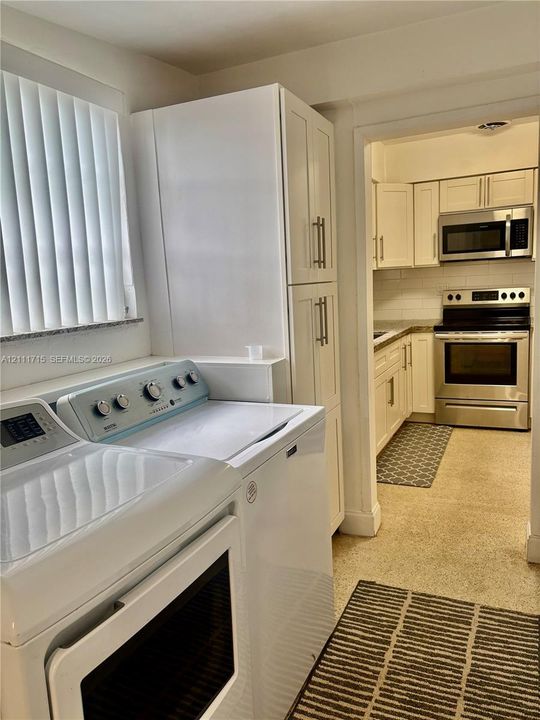 Laundry area featuring floor-to-ceiling white cabinetry, complemented by a kitchen equipped with white shaker-style cabinets, stainless steel appliances, and a tiled backsplash