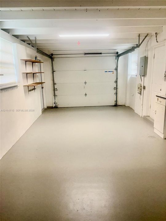 Garage featuring a sectional overhead door, painted concrete flooring, exposed ceiling beams, built-in shelving, and integrated lighting