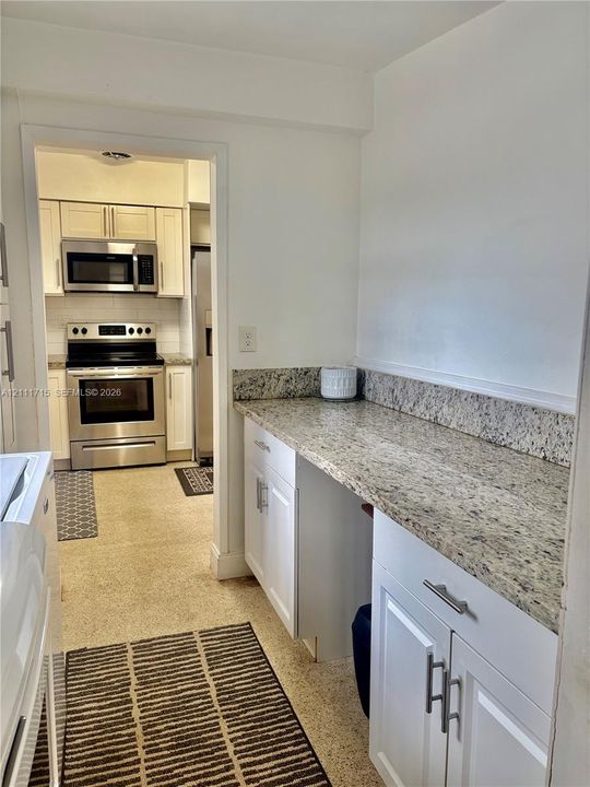 Kitchen featuring stone-finish countertops, white cabinetry with metallic hardware, and stainless steel appliances