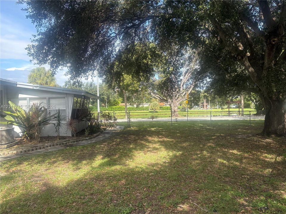 Expansive outdoor area featuring mature trees, a chain-link fence, and a stone walkway