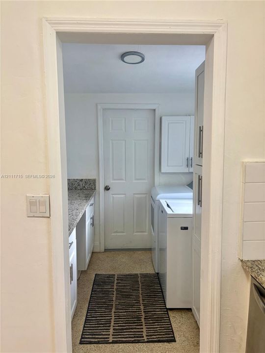 Laundry area featuring stone-look countertops, white shaker-style cabinetry, a built-in storage pantry, and a solid-core interior door