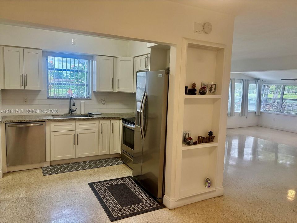 Kitchen featuring white cabinetry, stone-finish countertops, stainless steel appliances, tiled backsplash, and built-in wall shelving