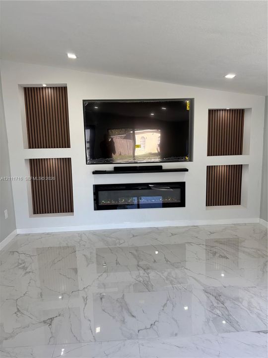 Custom built-in media wall featuring wood-slat accent paneling, recessed shelving, a sleek electric fireplace, and polished stone-finish flooring