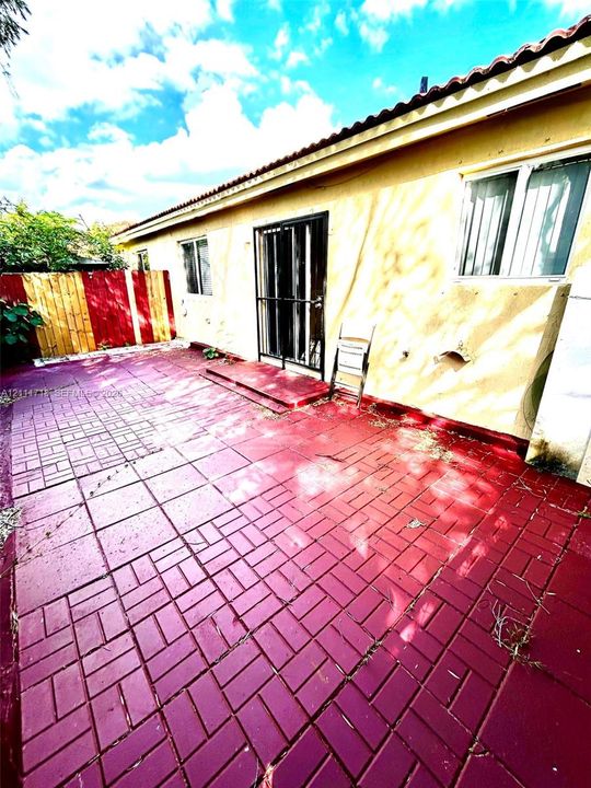 Exterior patio featuring stained concrete pavers, stucco siding, and a sliding glass door with a metal security gate