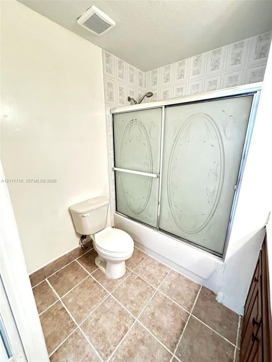 Bathroom featuring ceramic tile flooring, a tub-shower combination with sliding etched-glass doors, and decorative tile surround