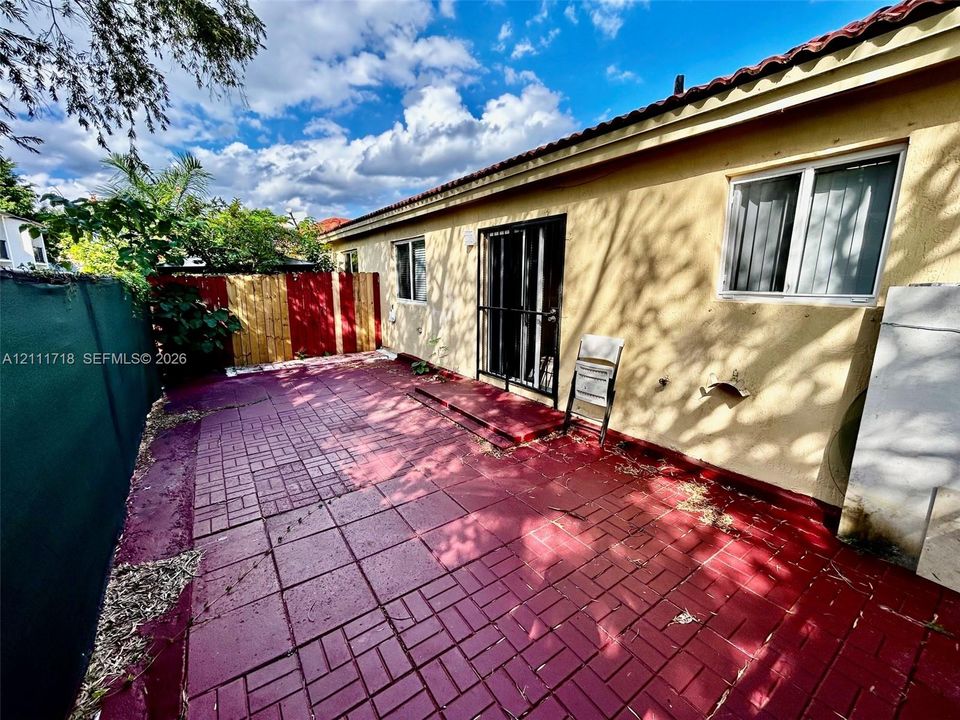 Exterior area featuring a paved patio, stucco siding, a tiled roof, and a metal security screen door