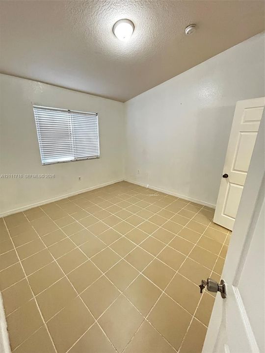 Room featuring neutral ceramic tile flooring, a window with installed horizontal blinds, a vaulted ceiling, and a paneled interior door with metal hardware