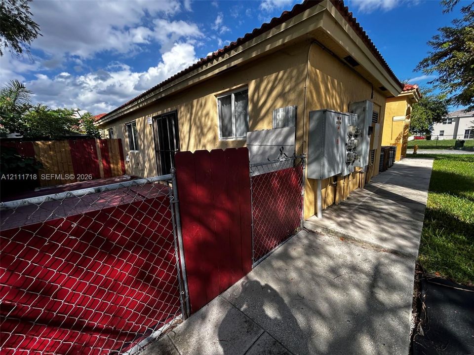 Stucco exterior featuring a clay tile roof, concrete walkway, and metal chain-link fencing with a privacy gate
