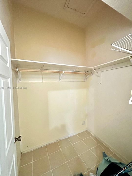 Storage area featuring tile flooring, ceiling-height shelving, and a horizontal hanging rod