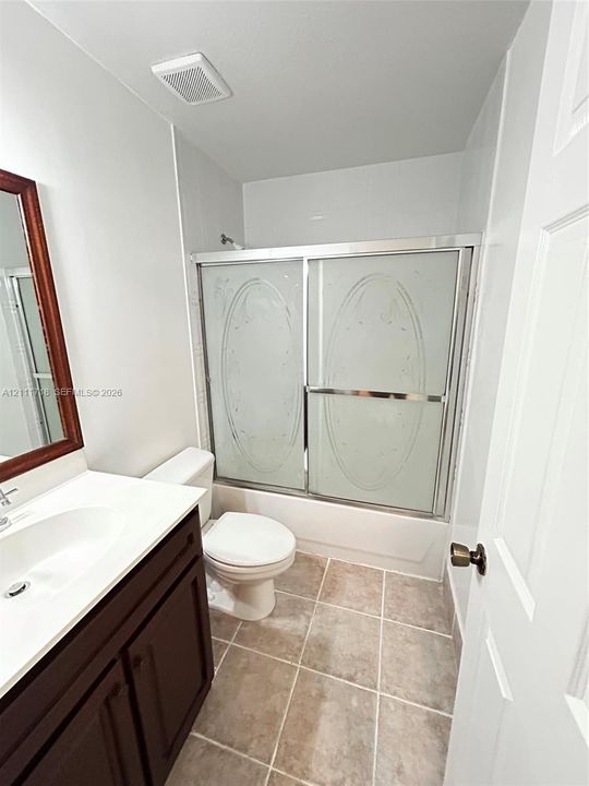 Bathroom featuring a dark wood-finish vanity, white countertop with an integrated sink, tiled flooring, and a tub-shower combination with sliding frosted glass doors