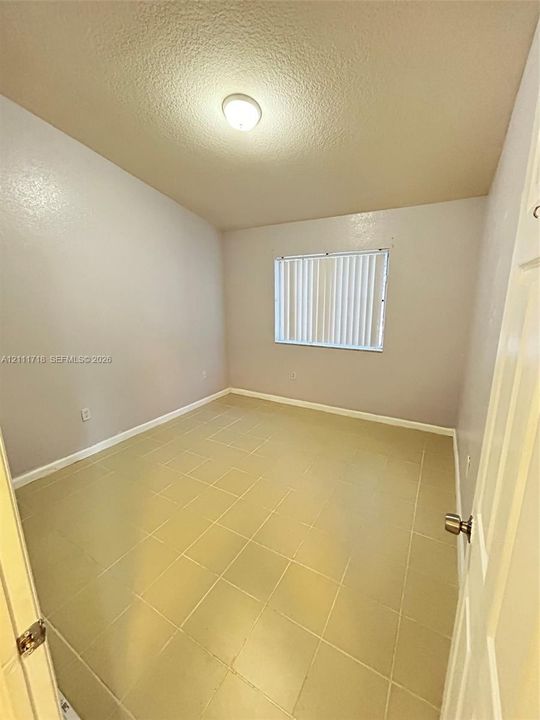 Interior room featuring neutral-toned tile flooring, light-colored walls, a ceiling-mounted light fixture, and a window with vertical blinds