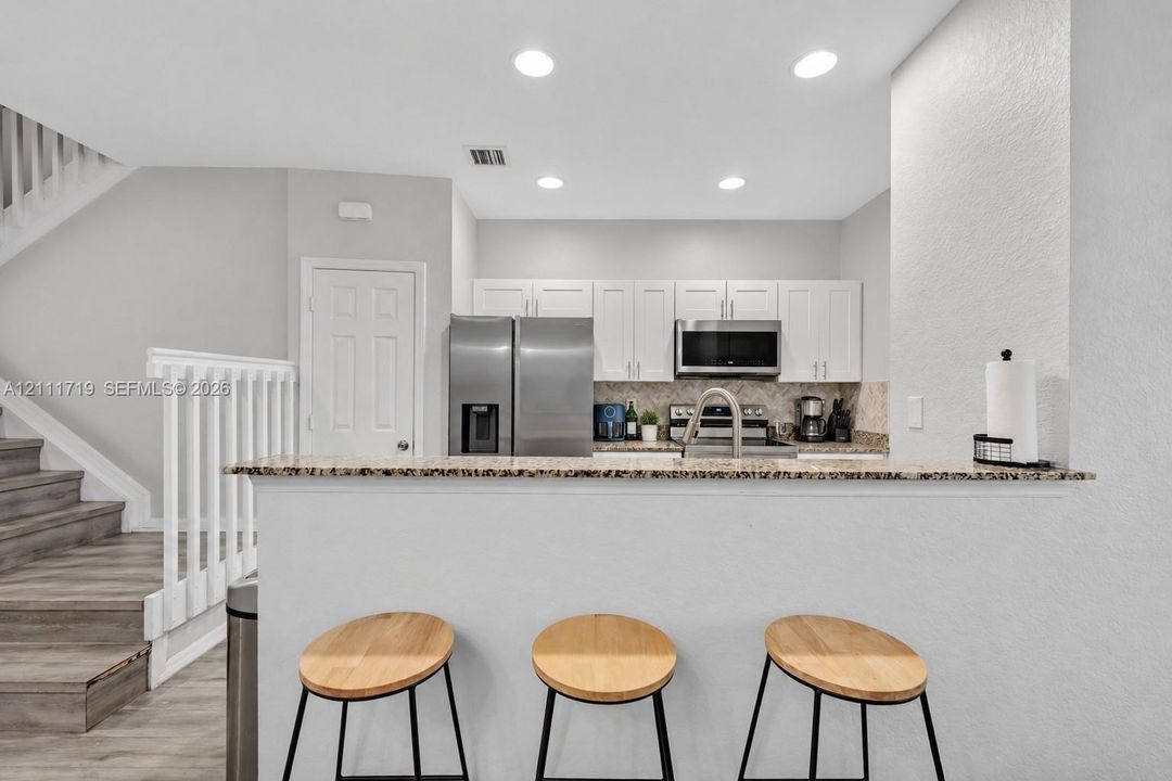 Kitchen featuring white shaker-style cabinetry, stone-finish countertops, stainless steel appliances, a breakfast bar, and recessed lighting