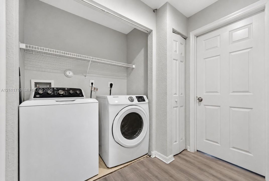 Laundry area featuring wood-finish flooring, a white-paneled interior door, bi-fold closet doors, and wire shelving