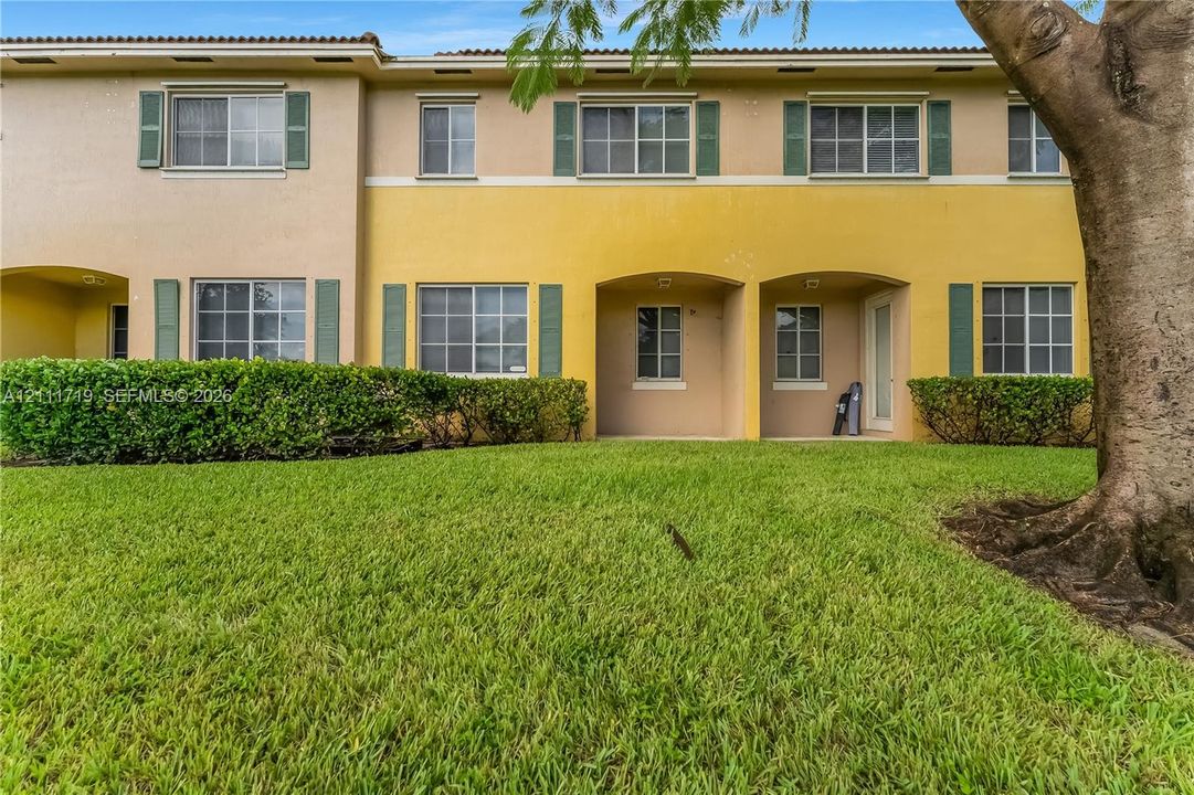 Two-story stucco exterior featuring covered ground-level patios, decorative window shutters, and a manicured lawn