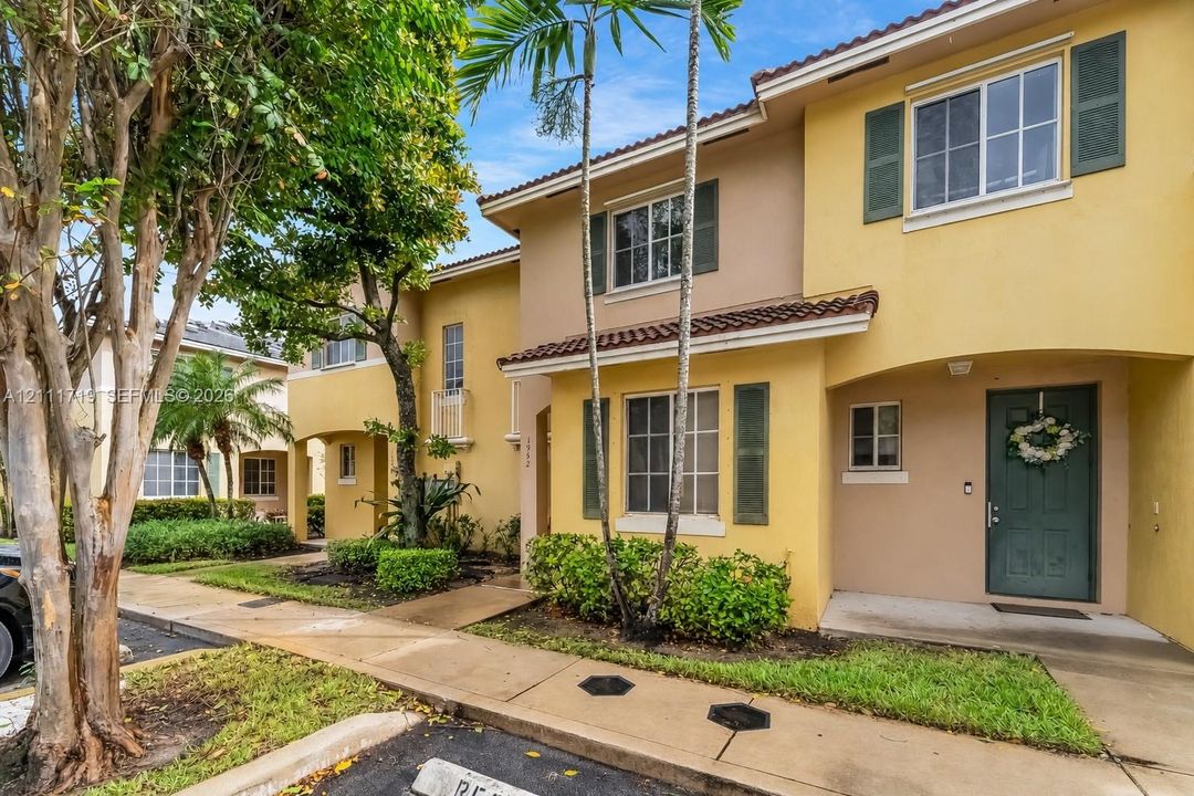 Two-story exterior featuring a stucco facade, tiled roof, decorative window shutters, and a concrete walkway