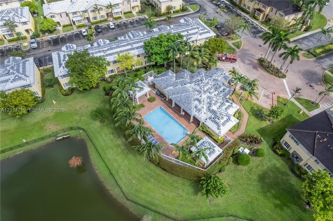 Aerial perspective of a multi-story residence featuring a private swimming pool, paved patio, detached pergola, and waterfront positioning
