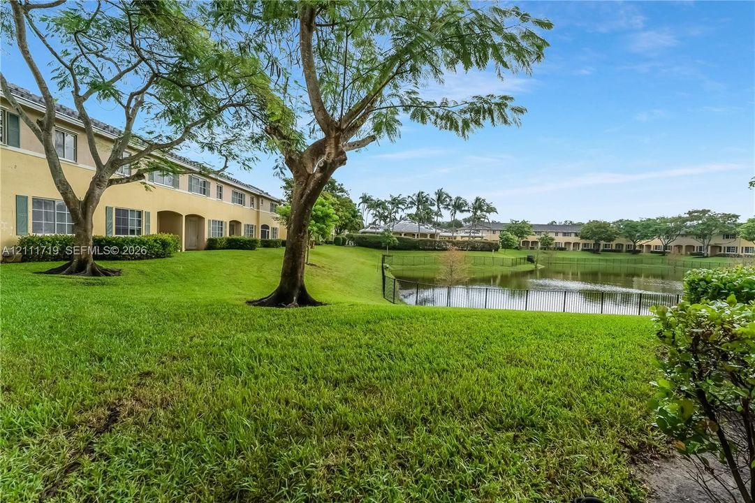 Waterfront grounds featuring a manicured lawn, mature trees, and perimeter fencing