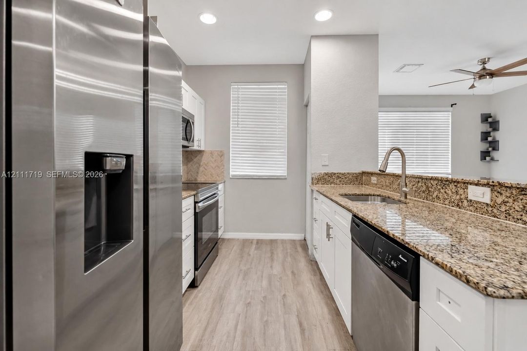 Kitchen featuring stainless steel appliances, white cabinetry, stone-finish countertops, herringbone-pattern backsplash, and wood-finish flooring