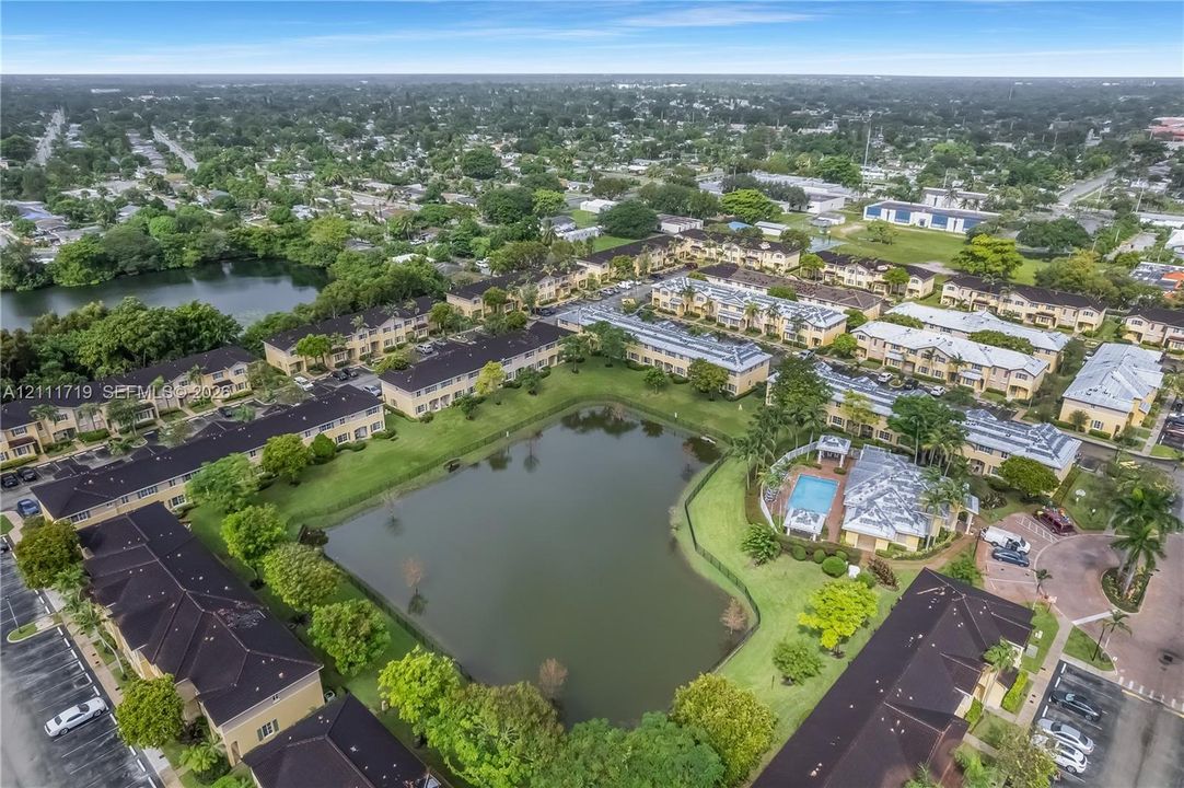 Aerial perspective of community featuring a central pond, landscaped grounds, a swimming pool, and dedicated parking areas