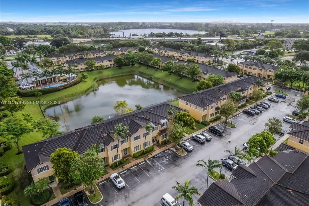 Aerial perspective of multi-unit residential buildings featuring dark tile roofing, stucco exterior walls, mature perimeter landscaping, and a central water feature