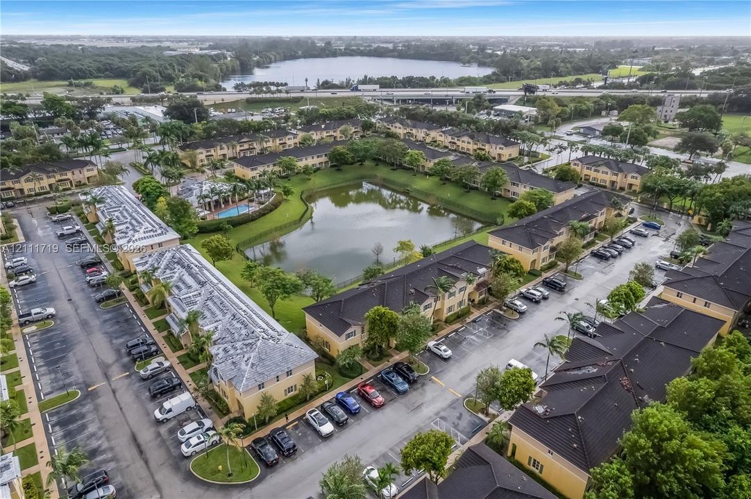 Aerial perspective of multi-unit residential buildings featuring dark-toned shingle roofing, central water feature, designated parking areas, and manicured landscaping