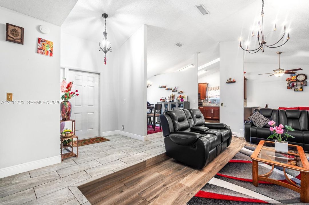 Open interior featuring vaulted ceilings, light-tone ceramic tile flooring, wood-finish flooring, and multi-arm chandelier lighting