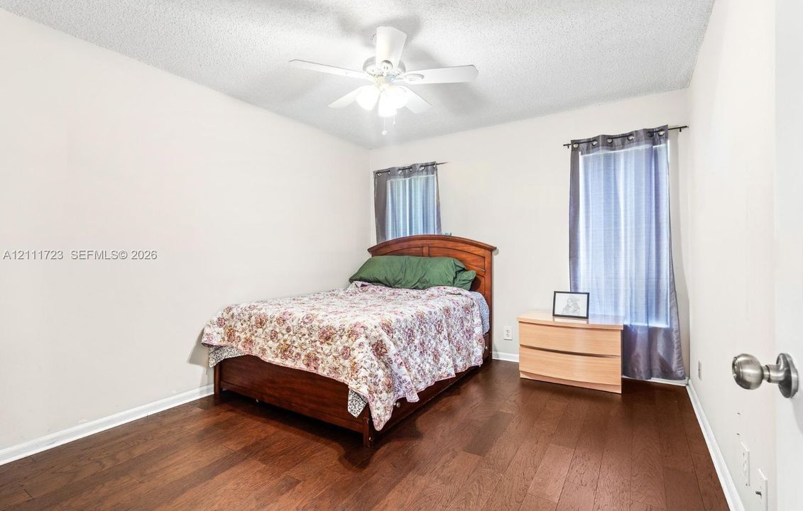 Room featuring wood-finish flooring, dual windows, and an overhead ceiling fan with integrated light fixture