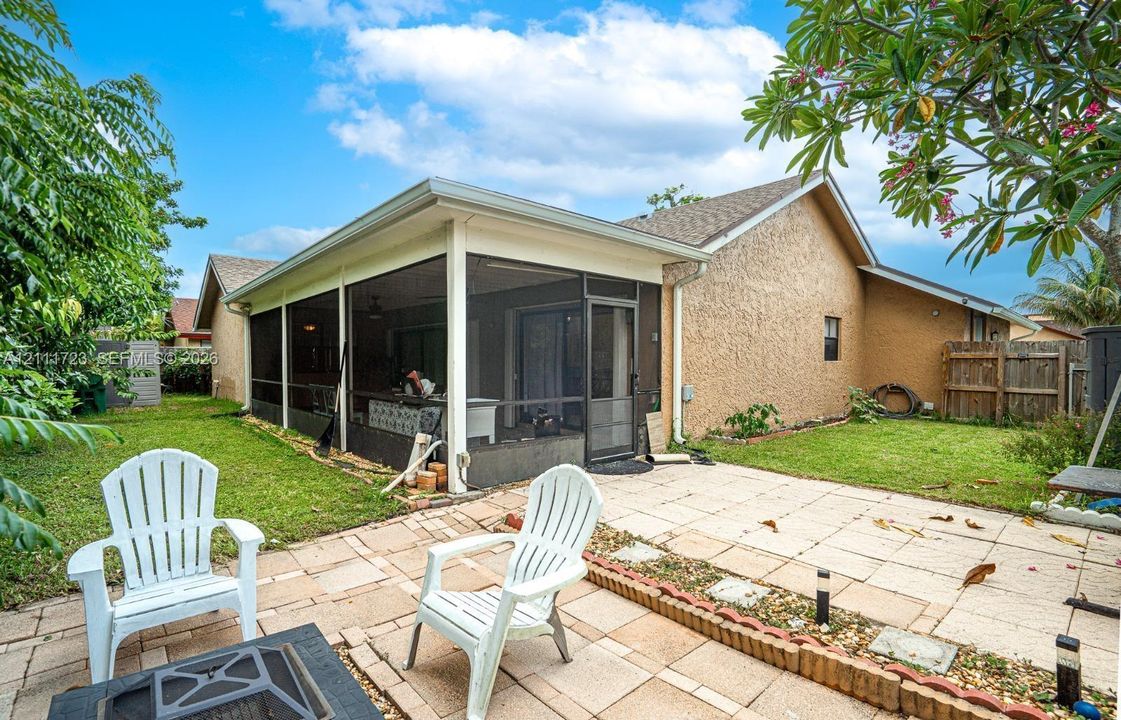 Rear exterior featuring a screened-in patio, concrete paver terrace, and grass lawn with a masonry border