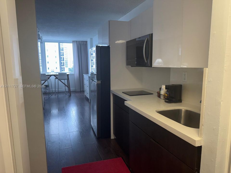 Kitchen featuring high-gloss white upper cabinetry, dark lower cabinetry, stone-finish countertops, stainless steel sink, and wood-finish flooring